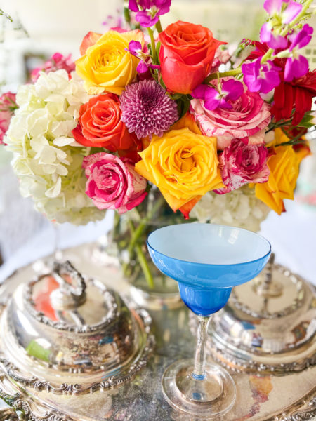 fancy silver lazy susan serving tray with colorful flowers in middle and a bright blue margarita glass