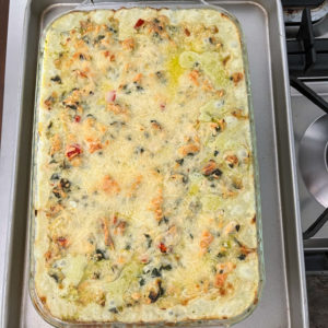 chicken casserole with spinach and artichokes in a 9x13 glass casserole dish on top of a cookie tray on a stove
