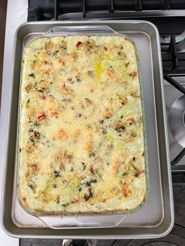 chicken casserole with spinach and artichokes in a 9x13 glass casserole dish on top of a cookie tray on a stove