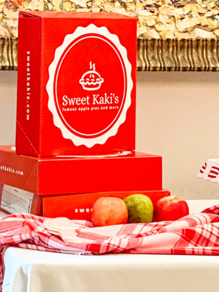 sweet kakis famous apple pie boxes stacked for display with plaid fabric and three apples beside boxes