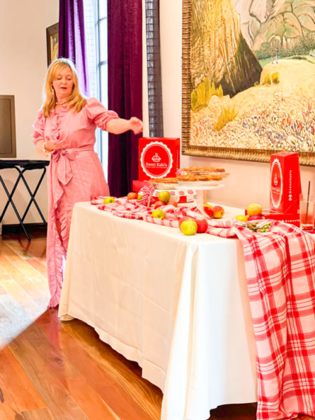 apple pie display with pink red and white tablecloths and red pie boxes with lady in pink dress presenting