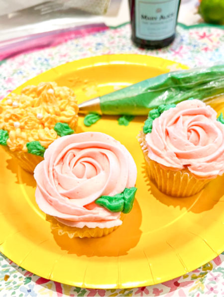 rose cupcakes in pink on yellow plate with tube of green icing