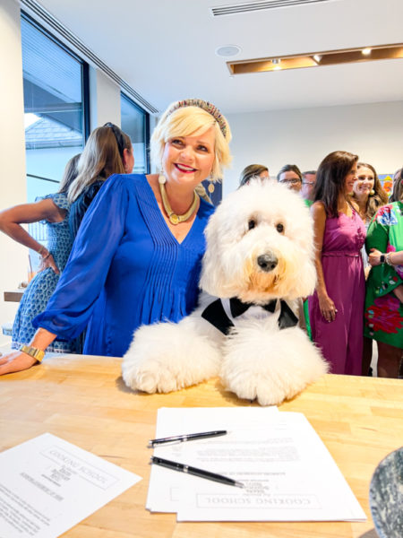 lady with blonde hair wearing a blue dress posing with white fluffy dog wearing a tuxedo vest