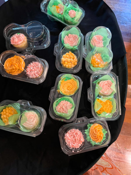 pink green and orange cupcakes in clear containers on black tray