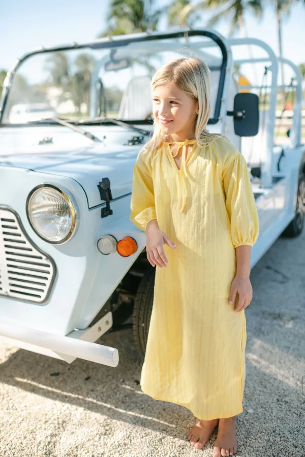 child standing beside moke car in yellow lemon print dress