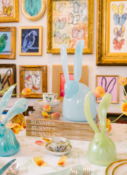 glass rabbit sculptures on table with colorful paintings on wall behind