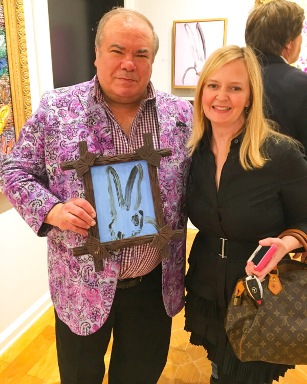 hunt slonem holding blue bunny painting with blonde lady beside him