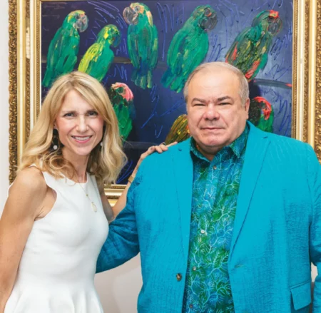 artist hunt slonem with art gallery owner jessica hagen standing in front of colorful painting of birds