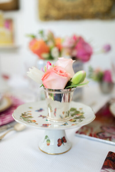 small cake stand with flowers and butterflies topped with silver cup of flowers