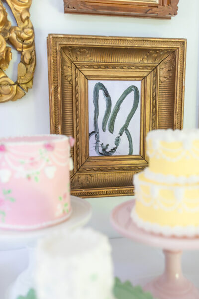 light lavender bunny painting in gold frame surrounded by pink and yellow cakes