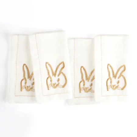 4 white dinner napkins with gold bunnies embroidered on them