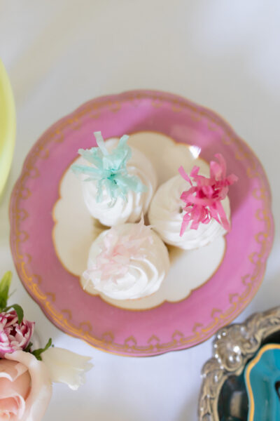 overhead shot of three white cupcakes with festive toppes on antique pink compote stand