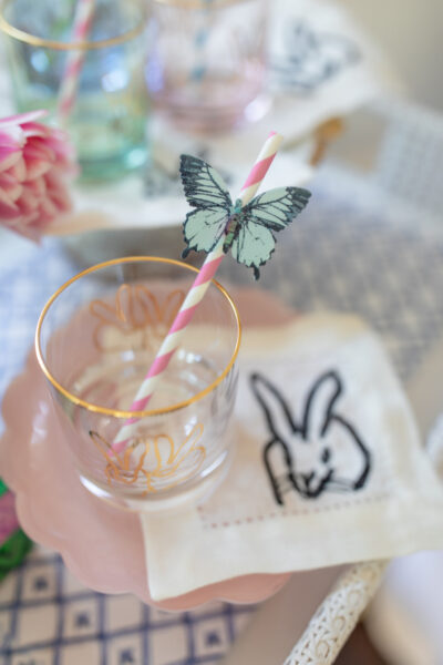 bunny glass with pink straw and wafer paper butterfly on straw and bunny cocktail napkin all on pink cake stand
