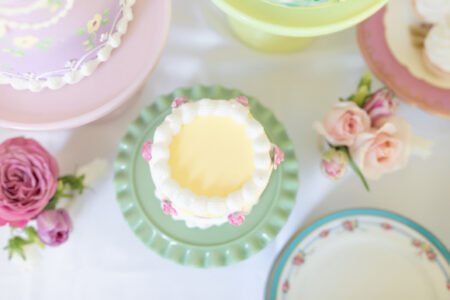 overhead shot of yellow mini cake surrounded by dessert plates flowers and other cakes